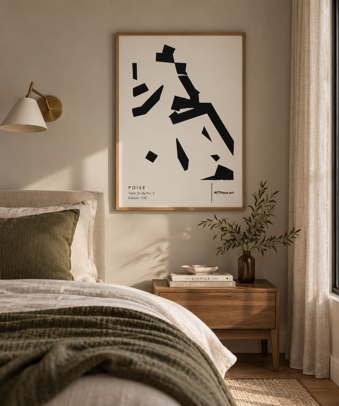 A framed abstract black-and-white art print hangs on a beige wall above a bed in a softly lit bedroom. The scene includes a wooden nightstand, books, a vase with branches, a wall lamp, and curtains.